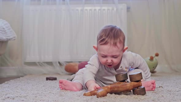 A happy child is playing with a wooden toy on the carpet in the nursery, age eight months