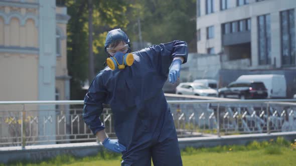 Funny Workout of Man in Respirator and Chemical Suit Outdoors. Portrait of Young Caucasian Sportsman alt