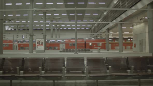Orange train departs an empty platform, lots of empty chairs; static shot alt