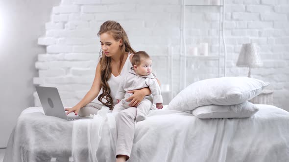 Confident Freelance Young Woman Working Typing Text on Laptop Pc During Holding Little Cute Child alt