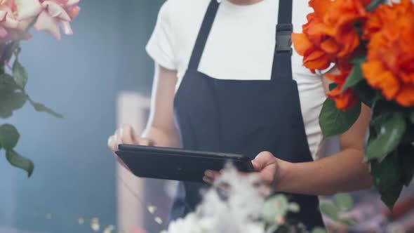 Female Florist Makes Inventory in a Flower Shop a Female Uses a Screen Tablet to Count the Number of alt