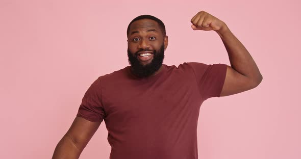 Young African American Man Demonstrate Biceps Isolated on Pink Background alt
