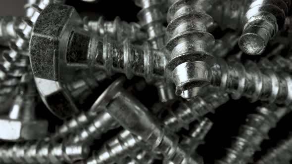 Pile of Steel Chrome Screws Rotating on Black Background alt