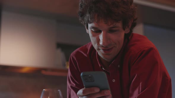 Positive Man Chatting on Mobile and Drinking Wine at Home alt
