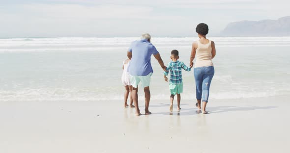 African american couple walking with children on sunny beach alt