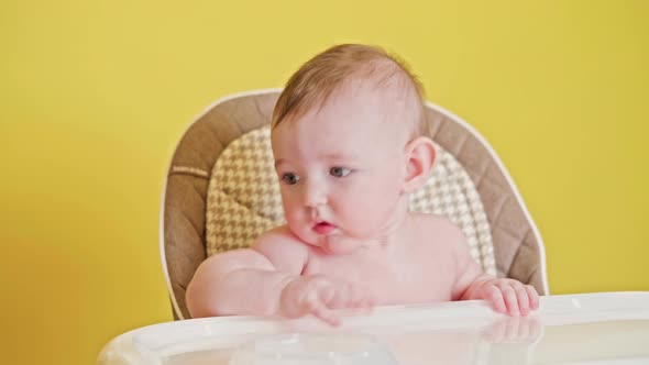 Mom feeding toddler baby from a spoon on a high chair for children, studio yellow background