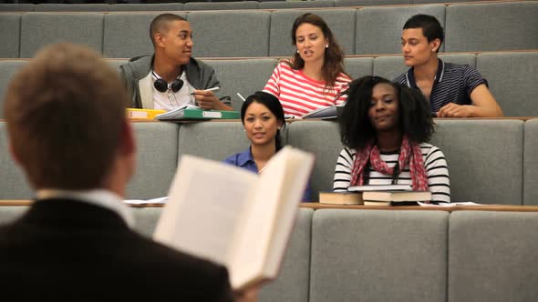 Teacher in front of students in lecture theatre reading literature alt