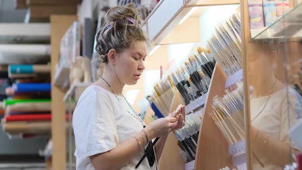 Woman Choosing Brushes for Drawing in Art Shop alt