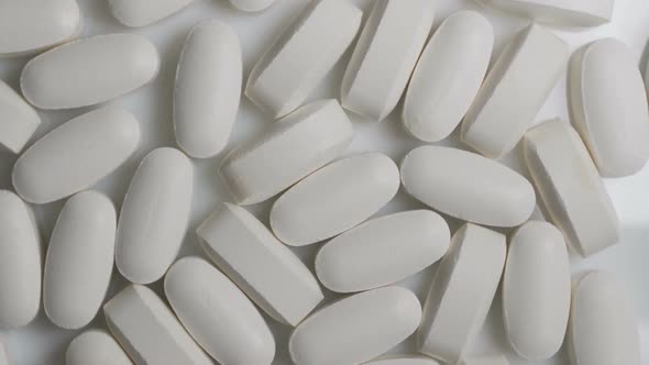 Close Up of White Capsules Rotate on Table. Pharmacy Antibiotic Pills alt