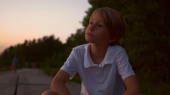 Closeup of a Blond Guy Sitting in a Park at Sunset alt