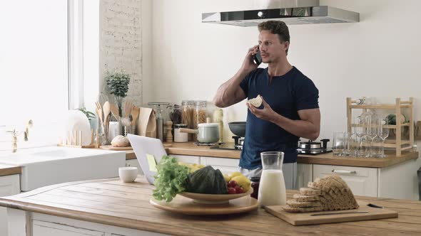 Casual man talking on the phone while having breakfast at home in kitchen
