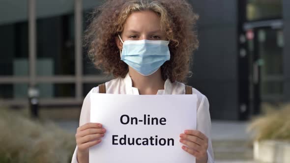 Schoolgirl Wearing a Medical Mask Holds a Sign ONLINE EDUCATION alt