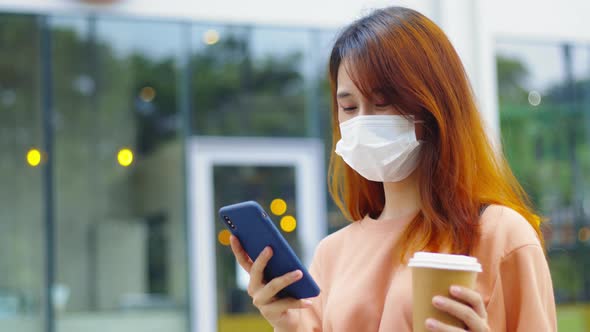 Young asian woman wear medical mask using a smartphone standing in the downtown street
