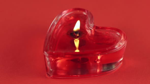 one heart shaped candle burning on red background alt