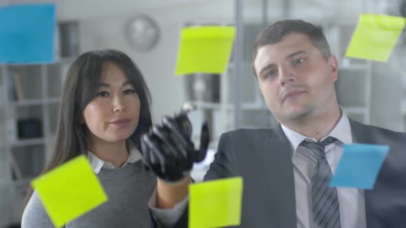Man with Bionic Hand Discussing Plans in Sticky Notes with Female Colleague alt