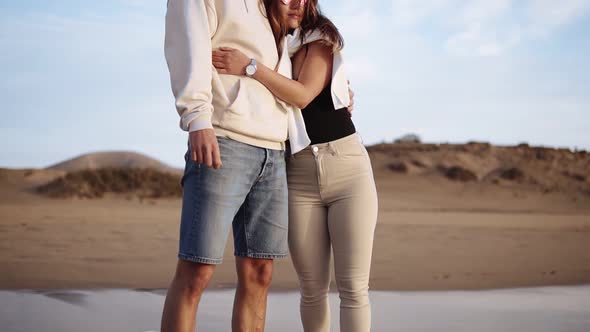 Stylish Young Couple Standing on Sandy Beach Shoreline Watch Sunset Waves From the Ocean alt
