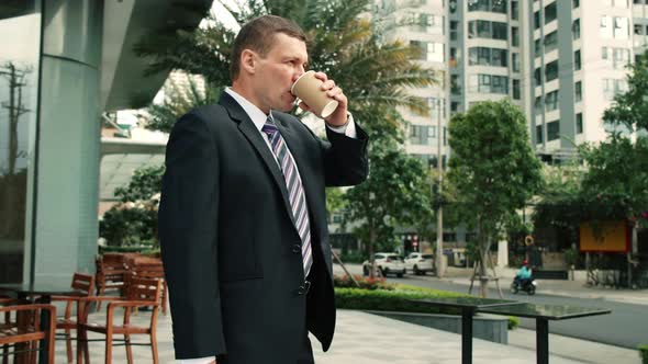 The Shot Moves Around a Businessman Standing on Street in the City Center Who and Drinks Hot alt