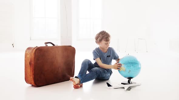 Boy looking at a globe while sitting beside a suitcase