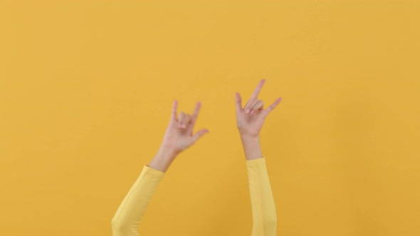 Woman hands doing I love you sign and waving around on isolated yellow studio background