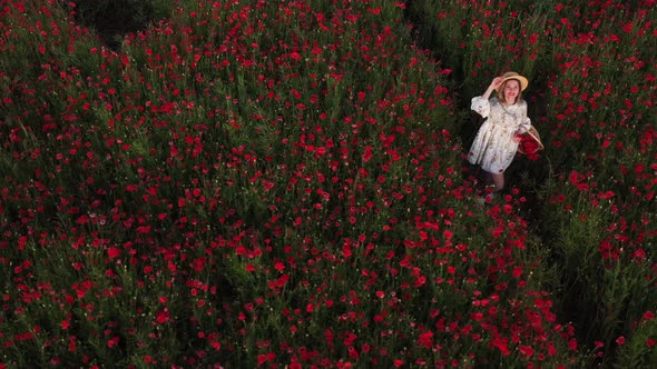 a Girl in a Dress with a Hat and with a Basket in a Field with Poppies