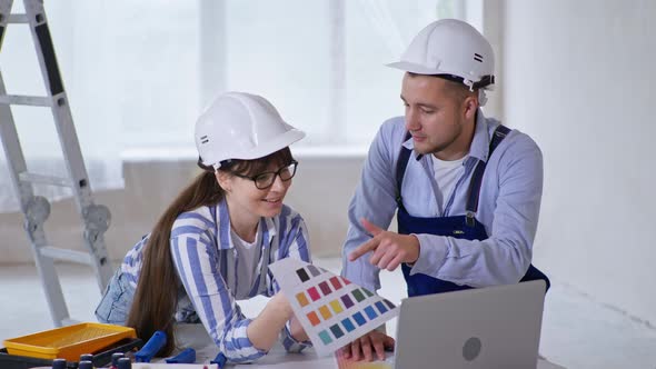 Professional Male and Female Builders in Protective Helmets and Colors in Their Hands Discuss Design alt