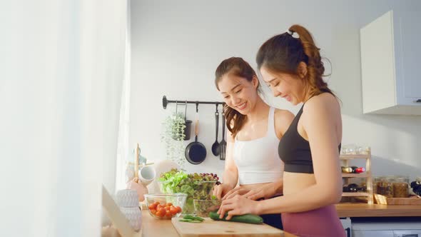 Asian young two women sibling in sportswear cooking salad in kitchen. alt