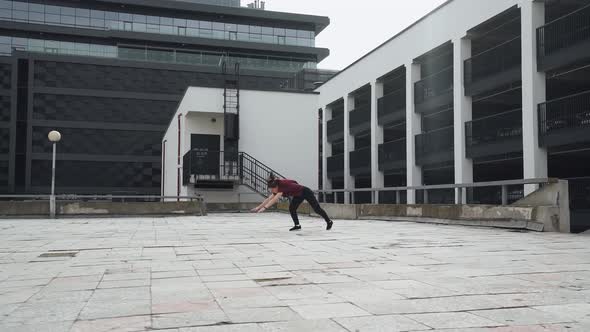 Young Female Gymnast Doing a Series of Flips on Training Area Near Modern Buildings alt