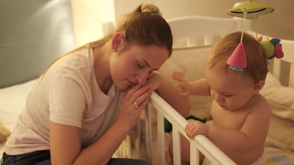 Tired Mother Fell Asleep Next to Her Baby Son Crib at Night alt