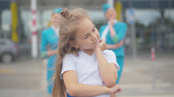 Portrait of Little Dreamy Girl Standing Next To Airport with Blurred Stewardesses at the Background alt