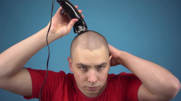 The Bald Young Man Insolently Shaves His Head. A Man Cuts His Hair Using a Hairdressing Machine on a alt