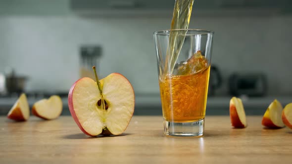 Filling glass with apple juice in the kitchen on wooden table with apple slices on background
