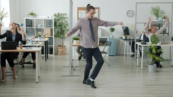 Creative Guy Performing Modern Dance in Office While Employees Having Fun in Background alt