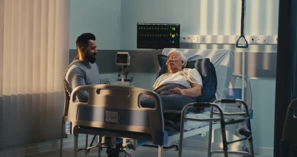Son Speaking with Senior Father in Hospital alt