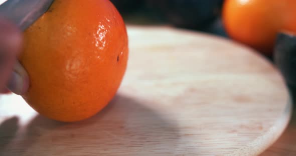 Close Still Shot of a Hand Grabbing a Clementine and Cutting it in Half With a Knife on a Wooden Sur alt