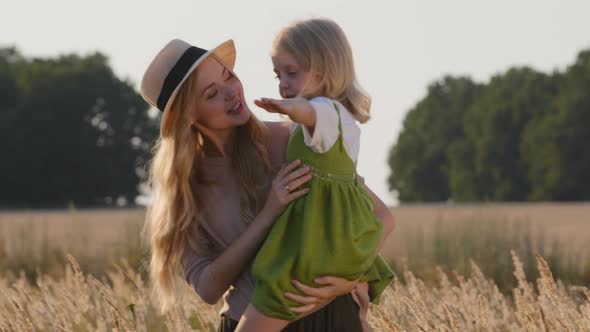 Young Woman Mother Caucasian Mommy in Hat Stands in Wheat Field Holding Small Girl Daughter Child alt