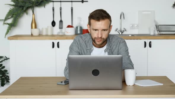 A Young Thoughtful Freelance Man Looking at A Monitor Screen, Working at a Computer alt
