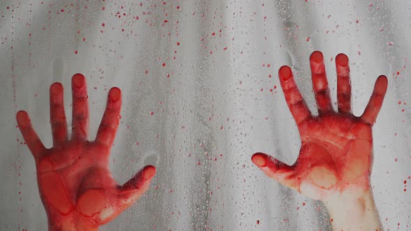Bloody hands on a white background. Behind a transparent glass covered with red drops. Close up alt