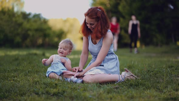 mother and baby sit in a park or in a forest on the ground looking at twigs and cones alt