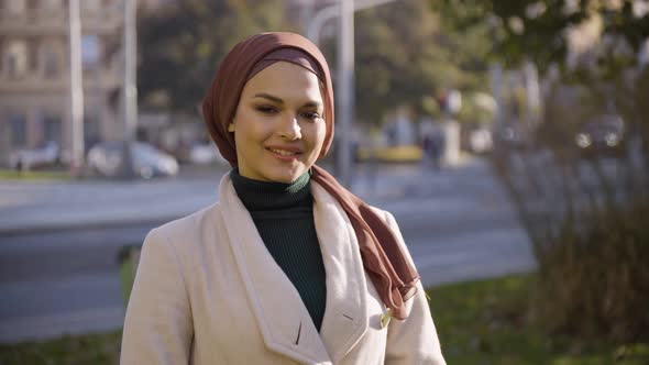 A Young Beautiful Muslim Woman Waves at the Camera with a Smile in a Park in an Urban Area  Closeup alt