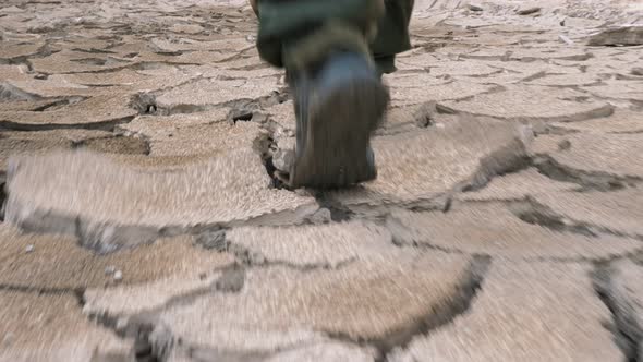 A Man in Boots Is Walking on Cracked Earth alt