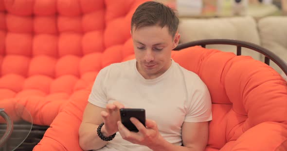 Man Is Chatting in the Smartphone Sitting in the Armchair