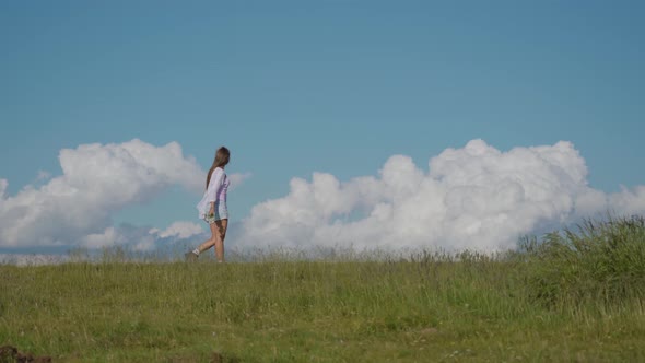 Girl Walks on the Green Grass with Blue Sky in the Background alt