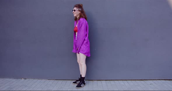fashionable girl in black glasses laughs against a gray wall alt