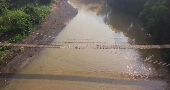 Sliding drone shot of suspension bridge over the river with motorcycle crossing on it in the morning alt