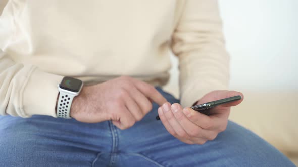 Cropped Male in Casual Wear Sit Using Smartphone at Home Thinking Indoors