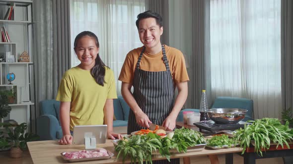 Asian Man Father And Daughter Looking And Smile To Camera While Cooking Together At Home alt