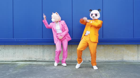Business couple wearing animal masks dancing in front of blue wall