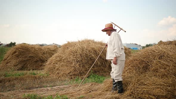 Tired Grandfather After Hard Work Sits Down on a Haystack Rests Wipes Sweat alt