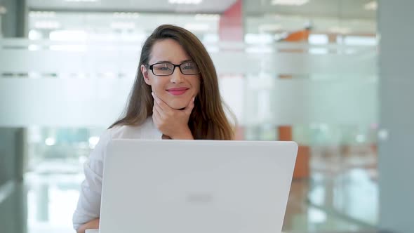 The Girl in a Spacious Bright Office, at a Desk With a Laptop. He Looks at the Camera and Smiles alt