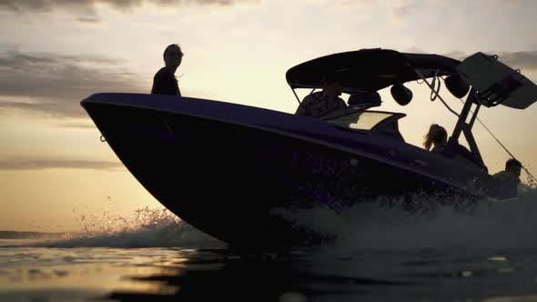 Speed Boat Or Wakeboat Silhouette Splashing Water During Sunrise Or Sunset